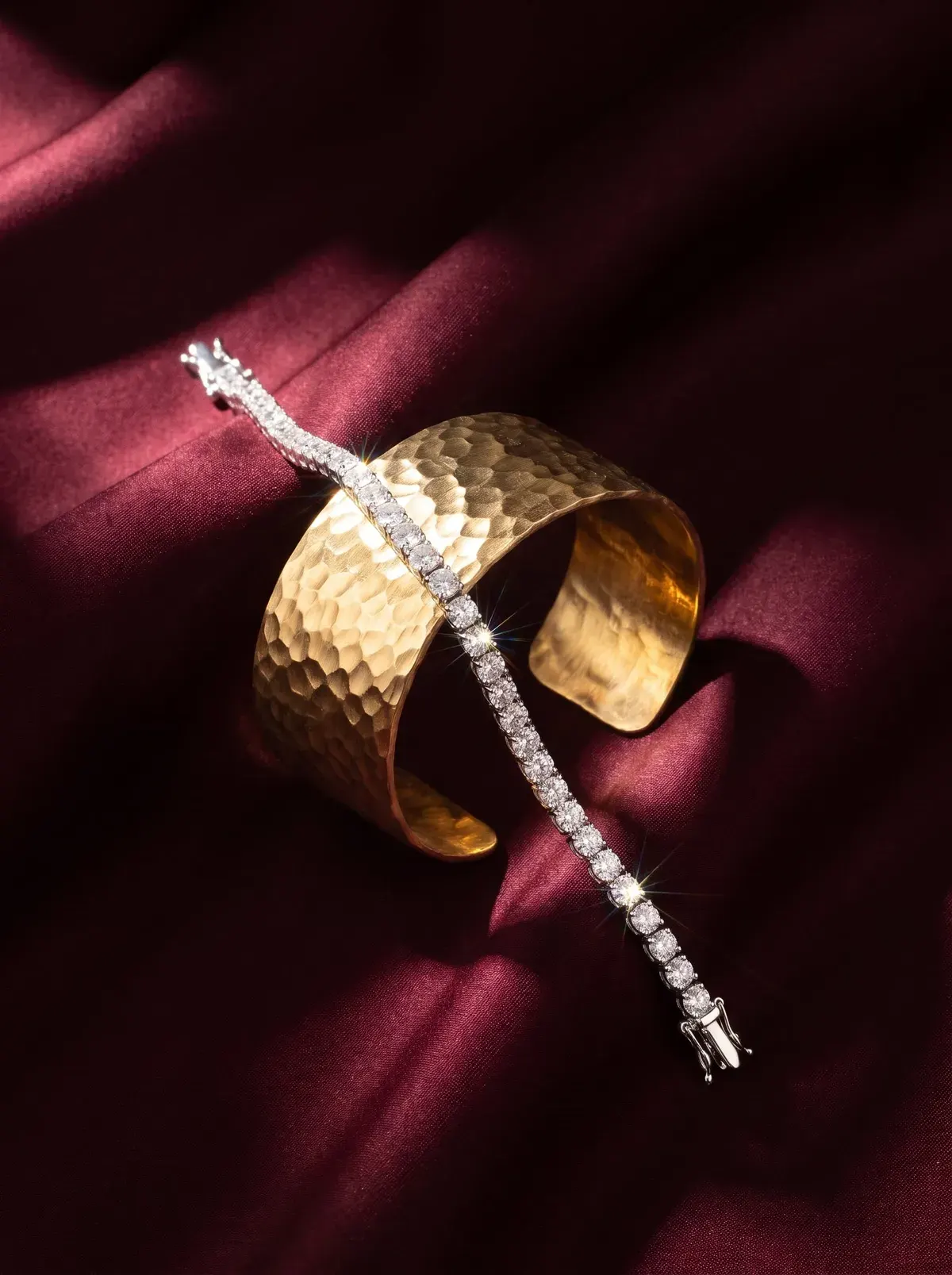 The hammered gold cuff and a diamond tennis bracelet on dark red satin
